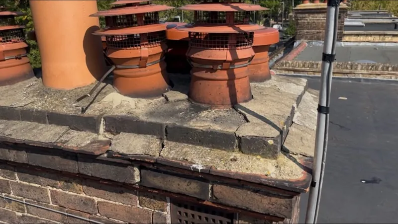 Brick chimney stack with a row of clay chimney pots fitted with cowls, beside a flat roof