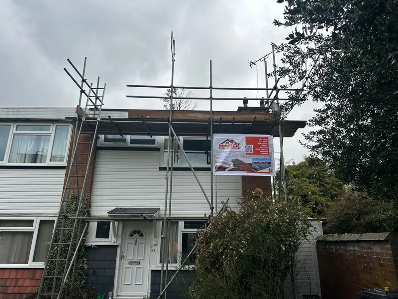 Scaffolding up to the roof edge of a clad end-terrace house, with a Nano Roofing & Guttering banner on the scaffold