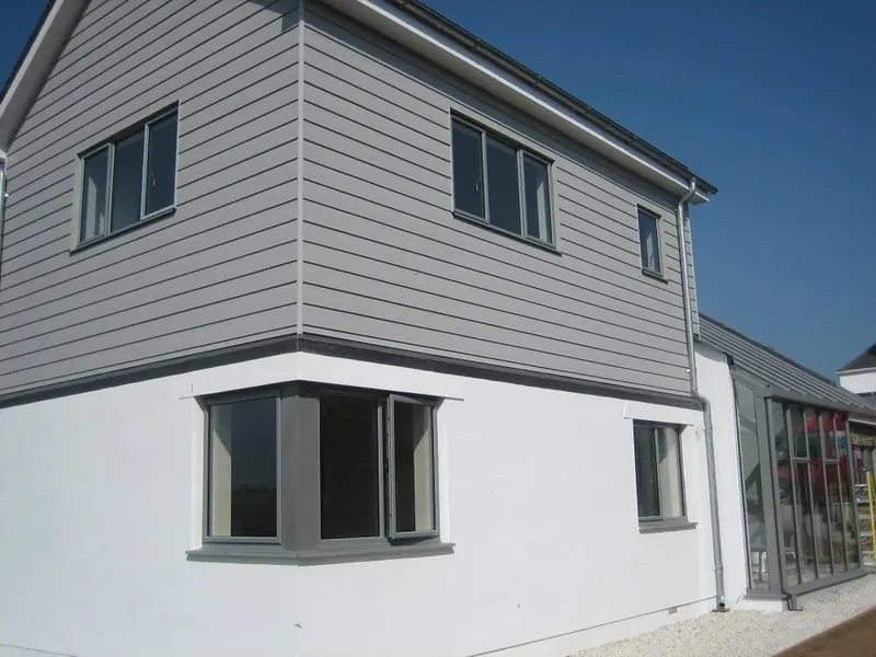 Two-storey house with grey horizontal cladding on the upper floor and white render below