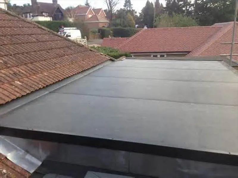 Black EPDM rubber flat roof beside a tiled pitched roof, with houses behind