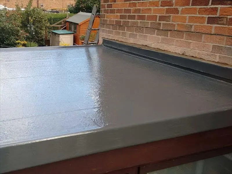 Close view of a glossy grey GRP flat roof finished against a brick wall