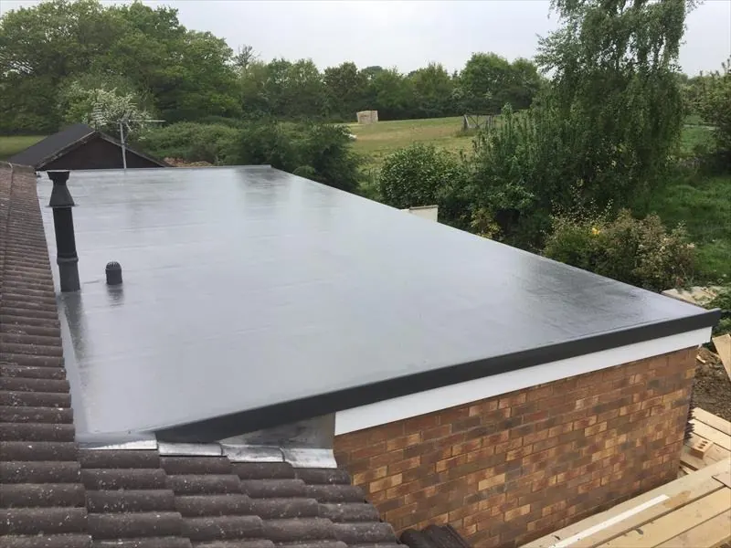 Charcoal GRP flat roof on a brick extension beside a tiled roof, with trees behind