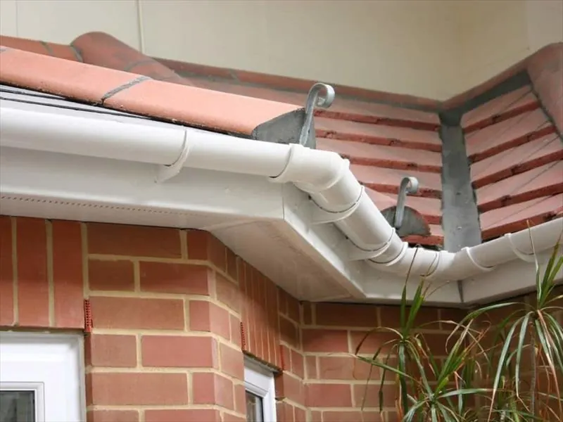White uPVC gutter running round the corner of a red brick bay below a tiled roof