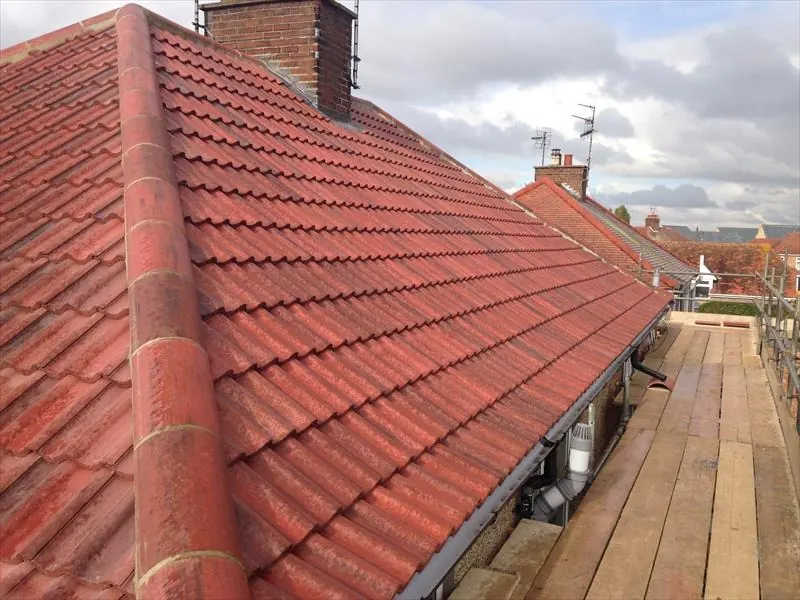 Red concrete tiled roof with ridge tiles along the top and a chimney stack, seen from scaffolding