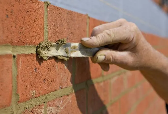 Hand using a pointing trowel to fill the mortar joints in a red brick wall