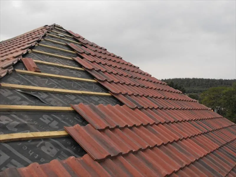 Red concrete roof tiles being laid over new battens and breathable membrane on a pitched roof